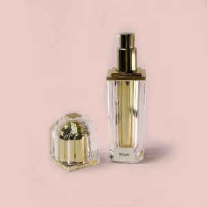 عطر مسك يظهر في زجاجة فاخرة بقلب ذهبي مع نزع الغطاء الشفاف ووضعه بجانبها على خلفية وردية ناعمة، موضحاً آلية الرش الذهبية.